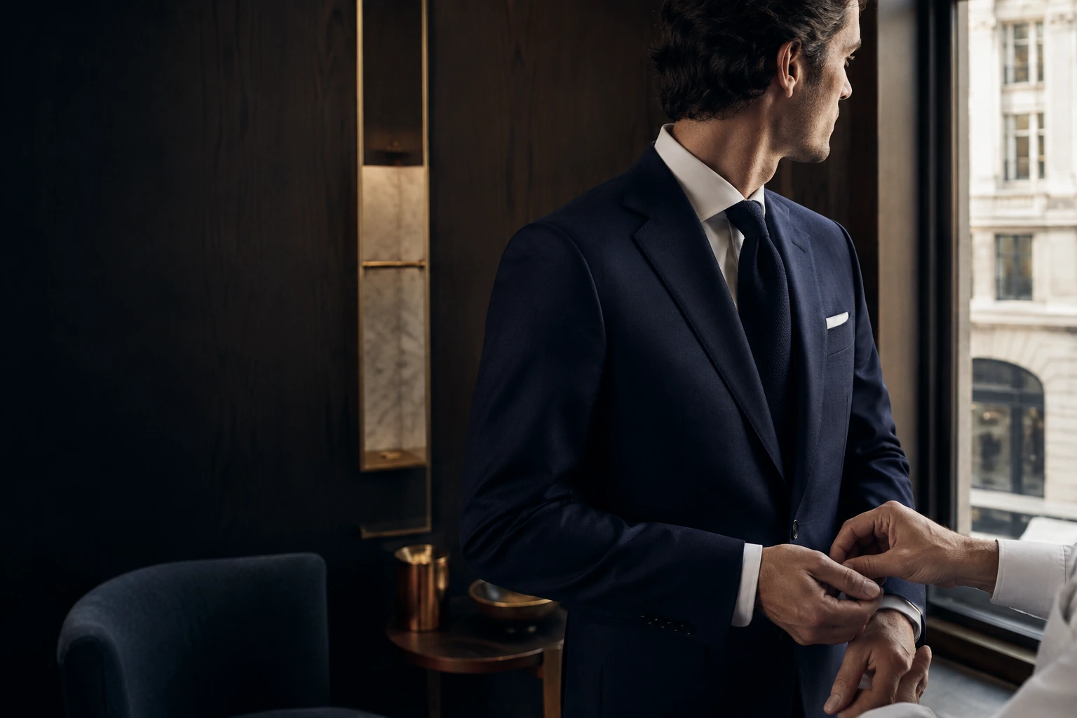 A client in a midnight navy suit receiving a private fitting beside a European window
